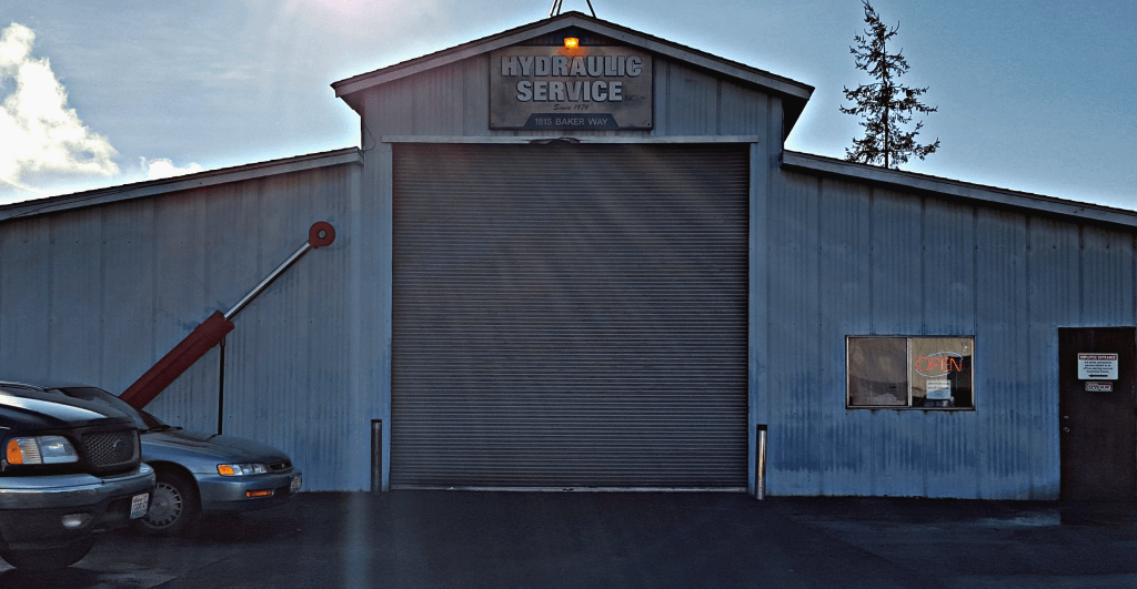 Hydraulic Service building with a closed garage door; a car and hydraulic cylinder visible.