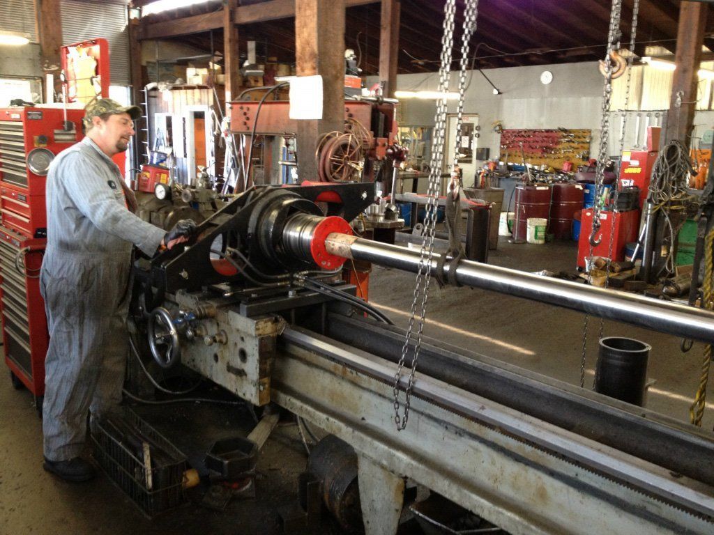 Mechanic operating a lathe machine in a workshop. He wears a worksuit, focused.