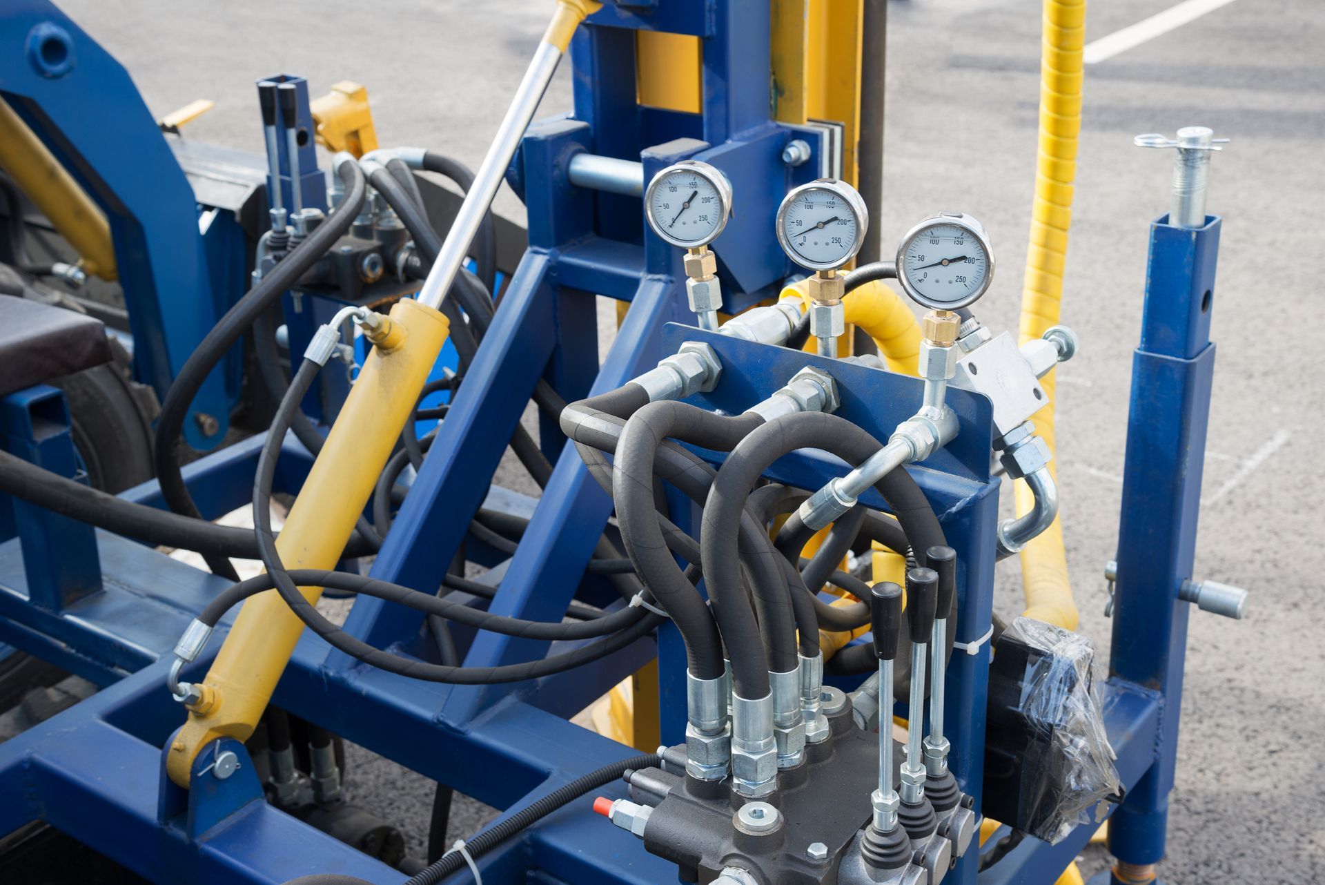 Blue and yellow machinery with gauges, hoses, and hydraulic cylinders.