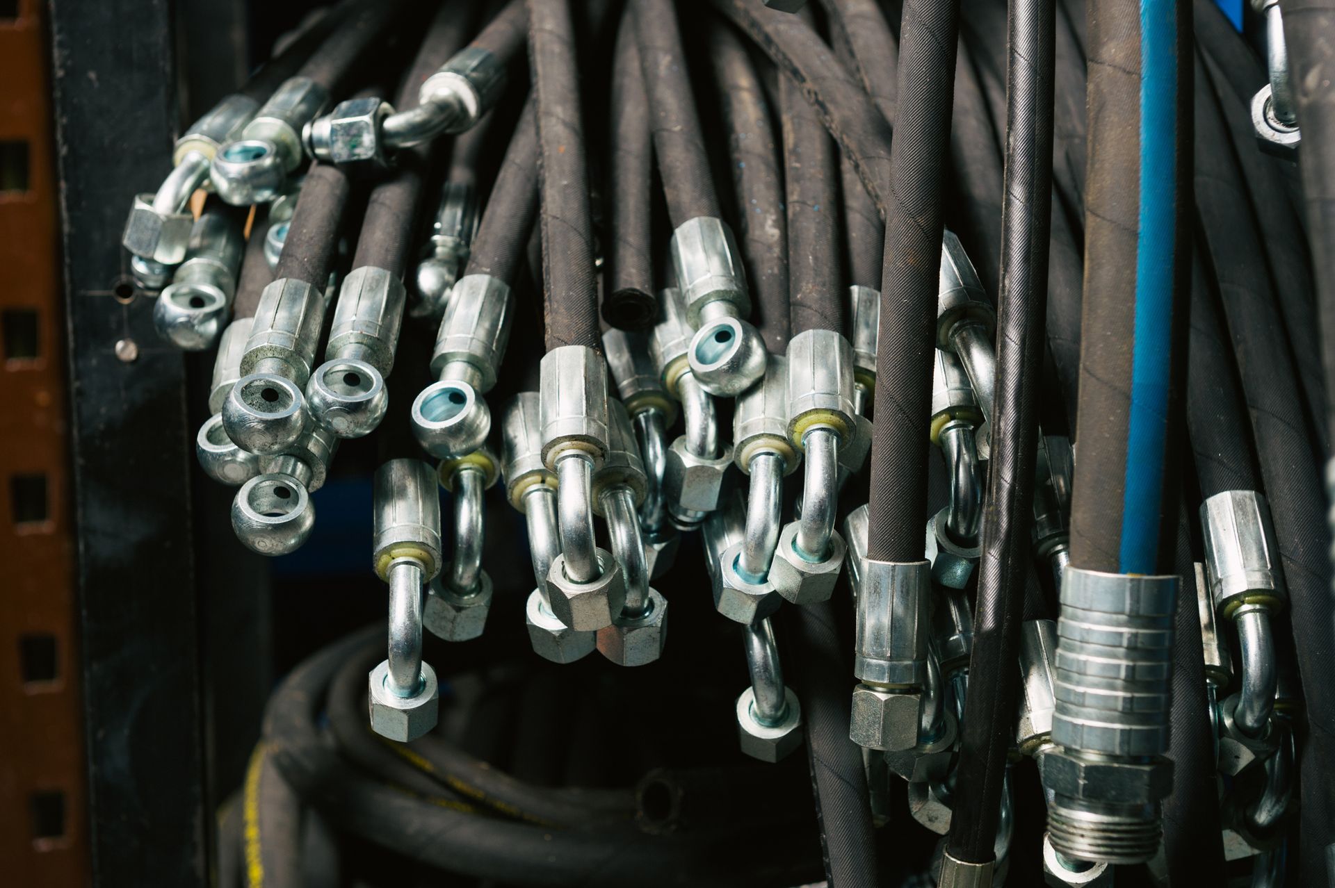 Black hydraulic hoses with metal fittings, hanging closely together.