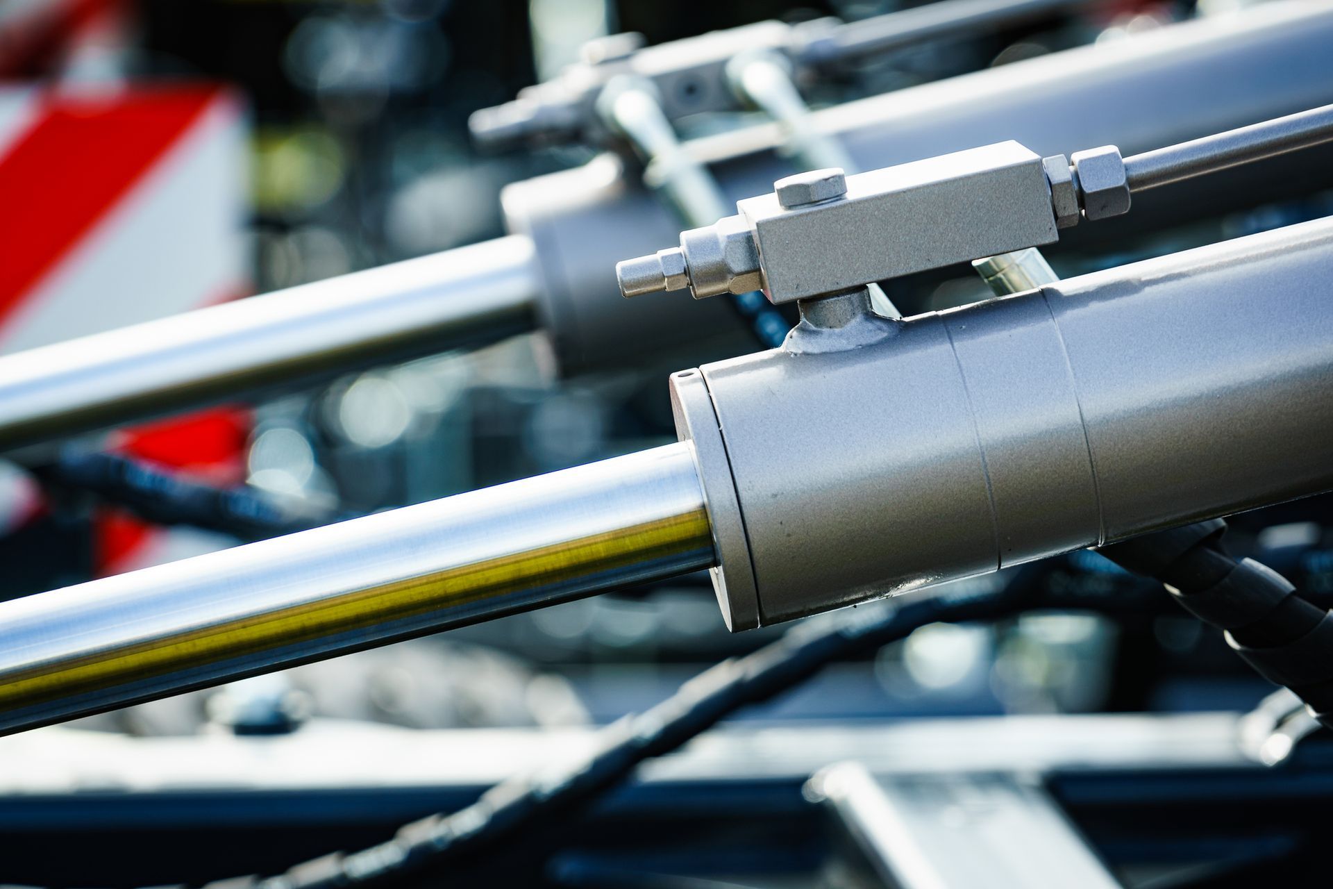 Silver hydraulic cylinders, likely on a vehicle, with connected hoses.