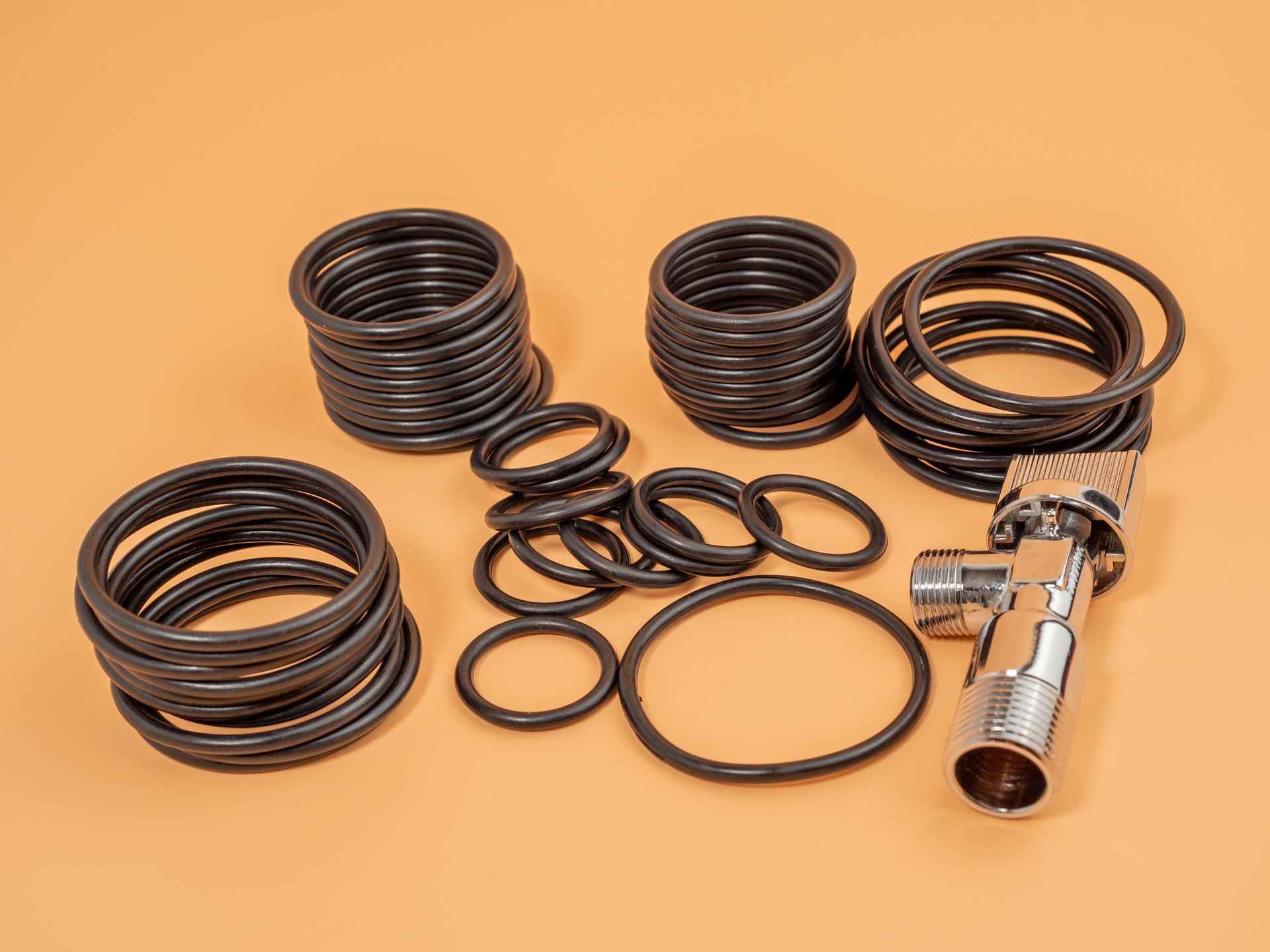 Various black O-rings and a silver plumbing fixture arranged on an orange surface.