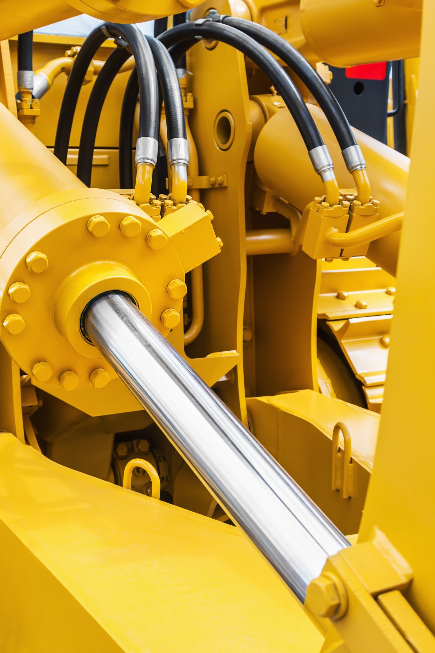Yellow hydraulic cylinder with black hoses on construction machinery.