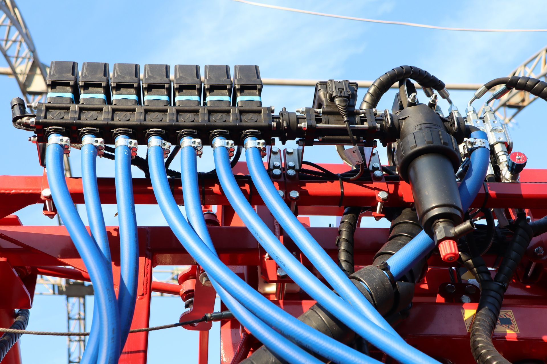 Close-up of agricultural equipment featuring blue hoses connected to a black manifold on a red frame.