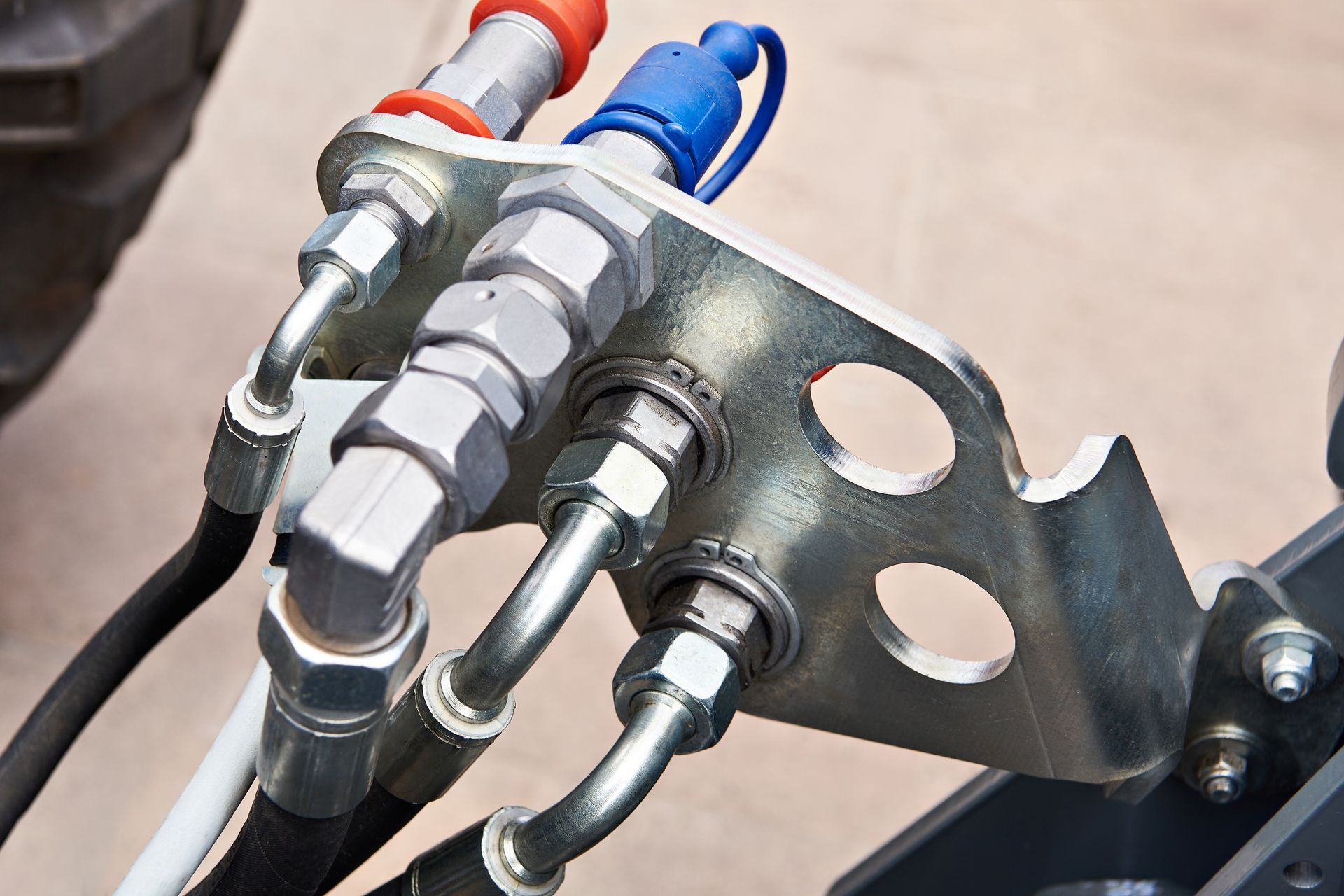 Hydraulic fittings with red and blue caps attached to a metal bracket.