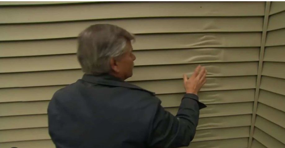 A photo of a man showing paint separation on a vinyl siding.