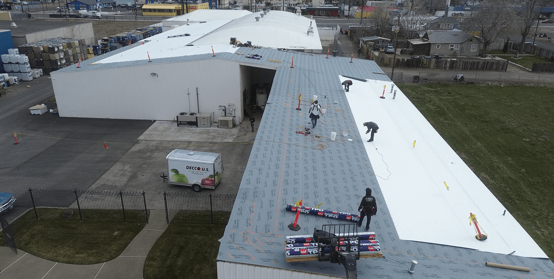 Aerial view of roofing crew installing TPO rolls and screwing plates over OSB substrate at Decco USA in Yakima.