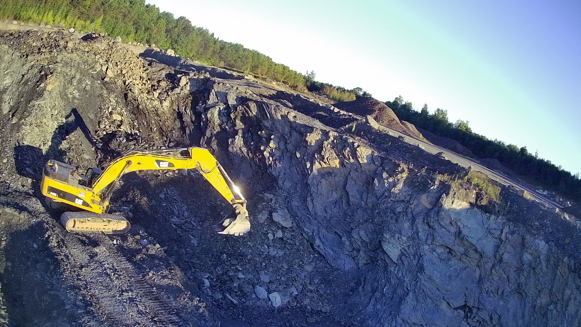 Une excavatrice jaune travaille sur une colline rocheuse.