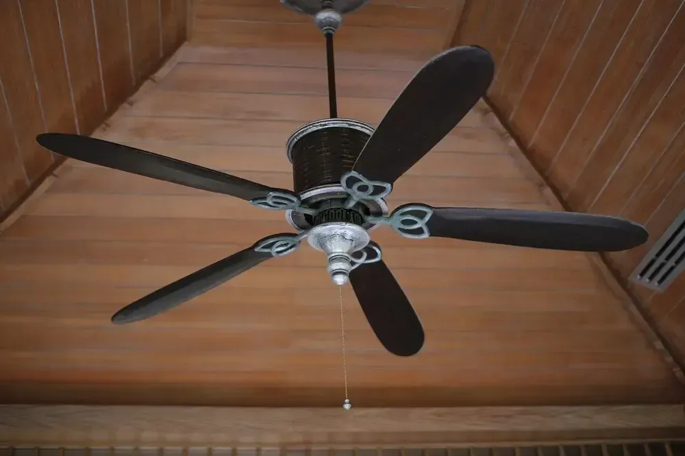 Ceiling fan with five dark brown blades, set in a wooden ceiling.