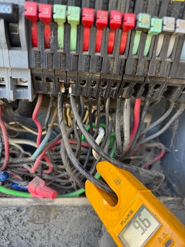 Close-up of electrical panel with a multimeter displaying 9.6. Wires and fuses are visible.