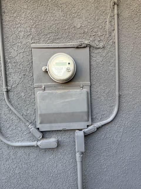 Gray electrical meter box on a textured wall with conduit pipes.
