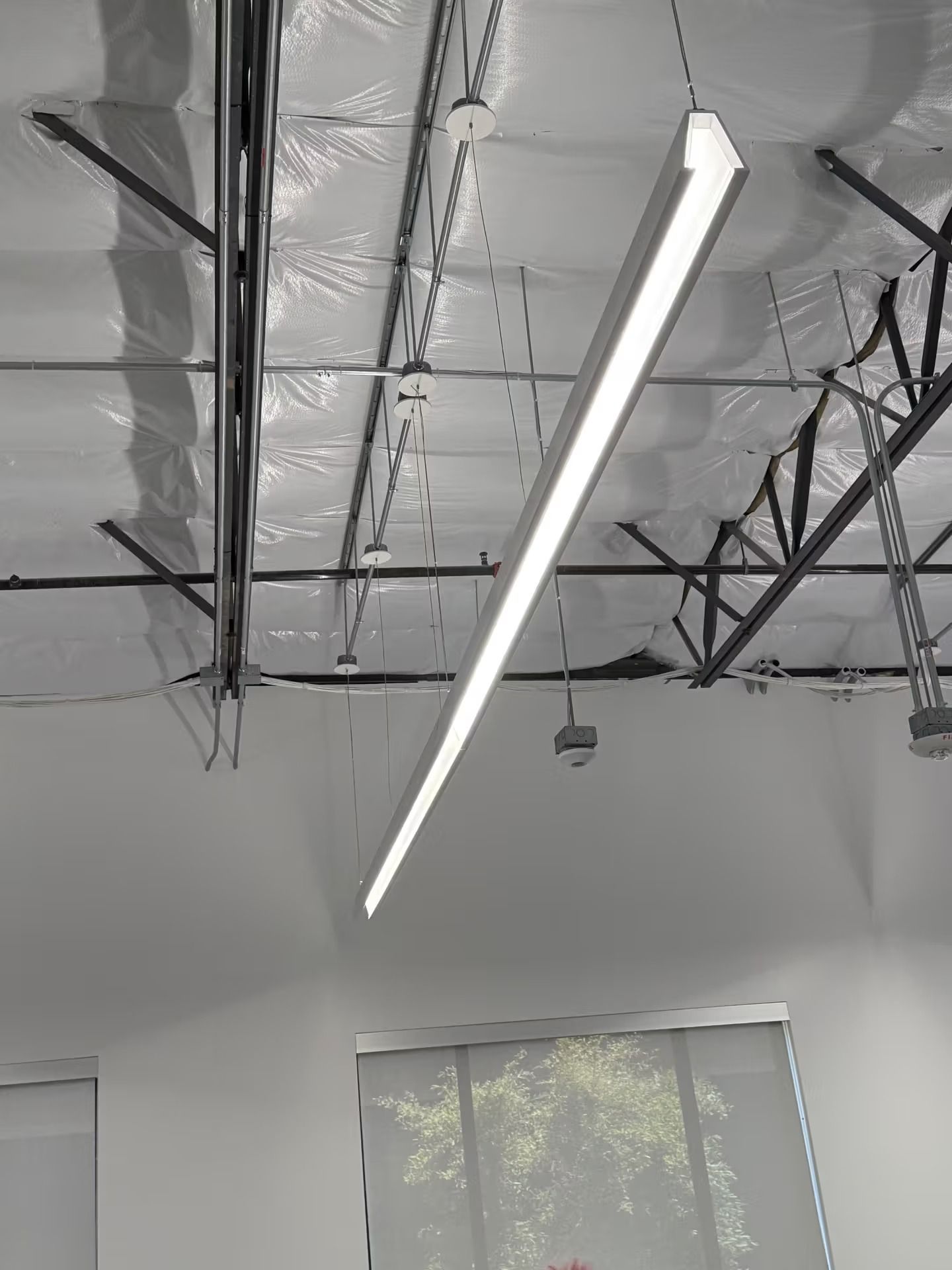 Long, rectangular LED light fixture suspended from a high ceiling in a room with industrial elements.