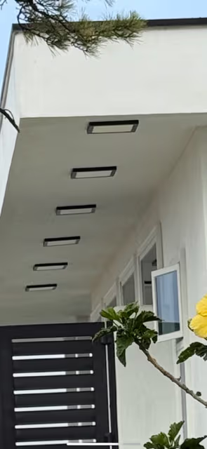 A white building with rectangular lights embedded in the ceiling. A black gate is in the foreground.