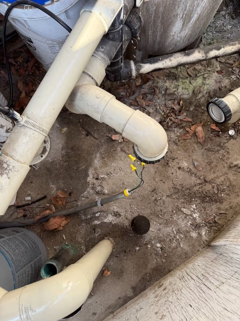 Pool plumbing with white pipes, electrical wiring, and a dark ball on the ground.