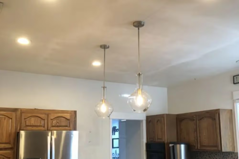 Two glass pendant lights hang over a kitchen with wooden cabinets and a stainless steel refrigerator.