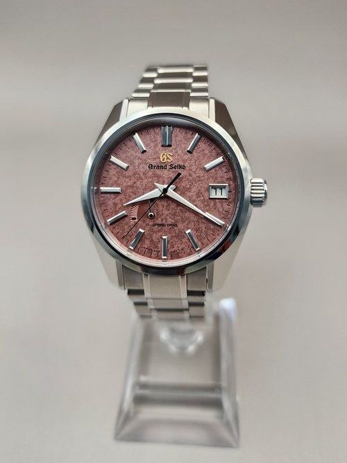 A silver watch with a red face is sitting on a clear stand.