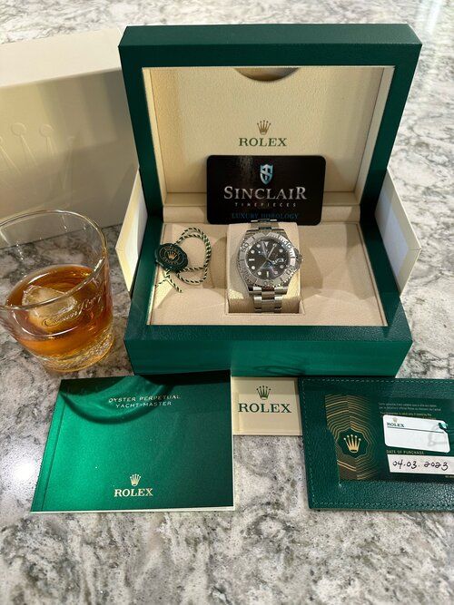 A rolex watch is in a box next to a glass of whiskey.