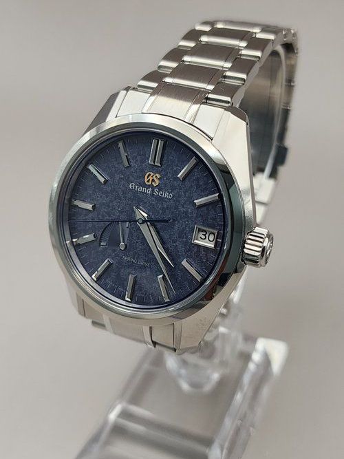A silver watch with a blue face is sitting on a glass display case.