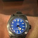 A person is wearing a black watch with a blue face on their wrist.