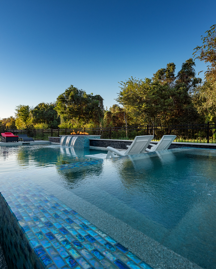 Blue-tiled outdoor pool with fountain jets and trees under a clear sky