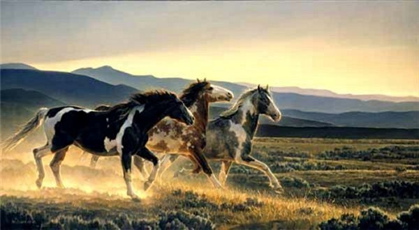 A herd of horses running in a field with mountains in the background.