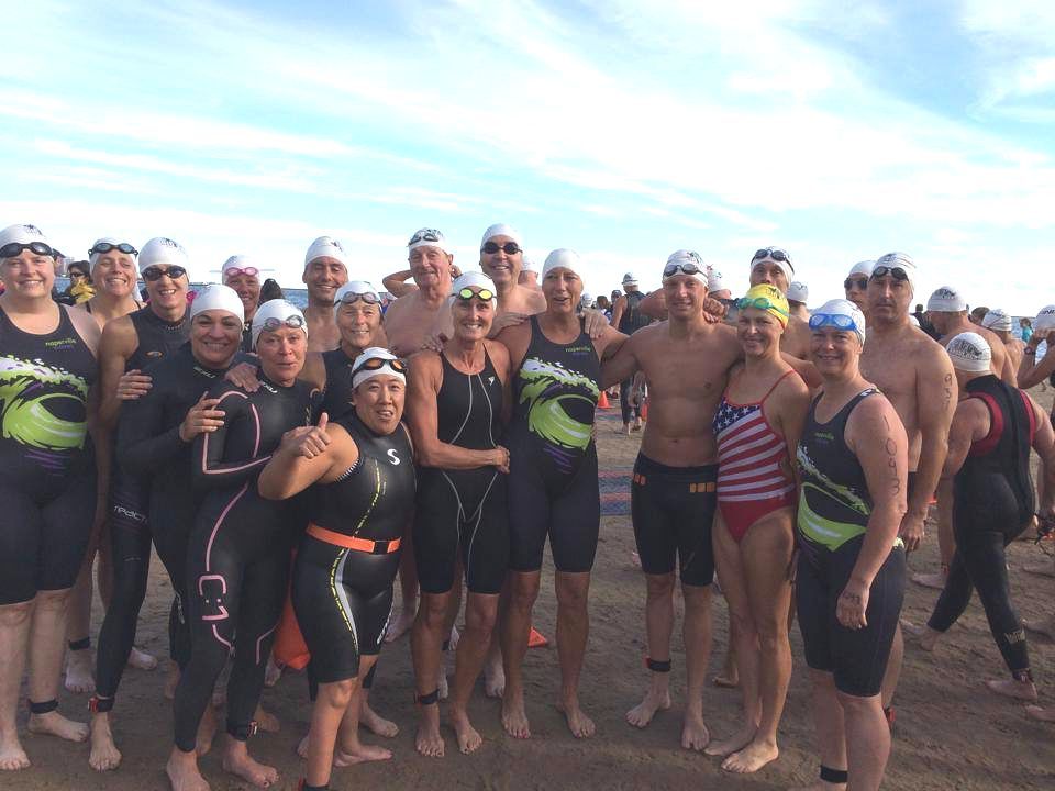 A group of people in wet suits and swim caps are posing for a picture
