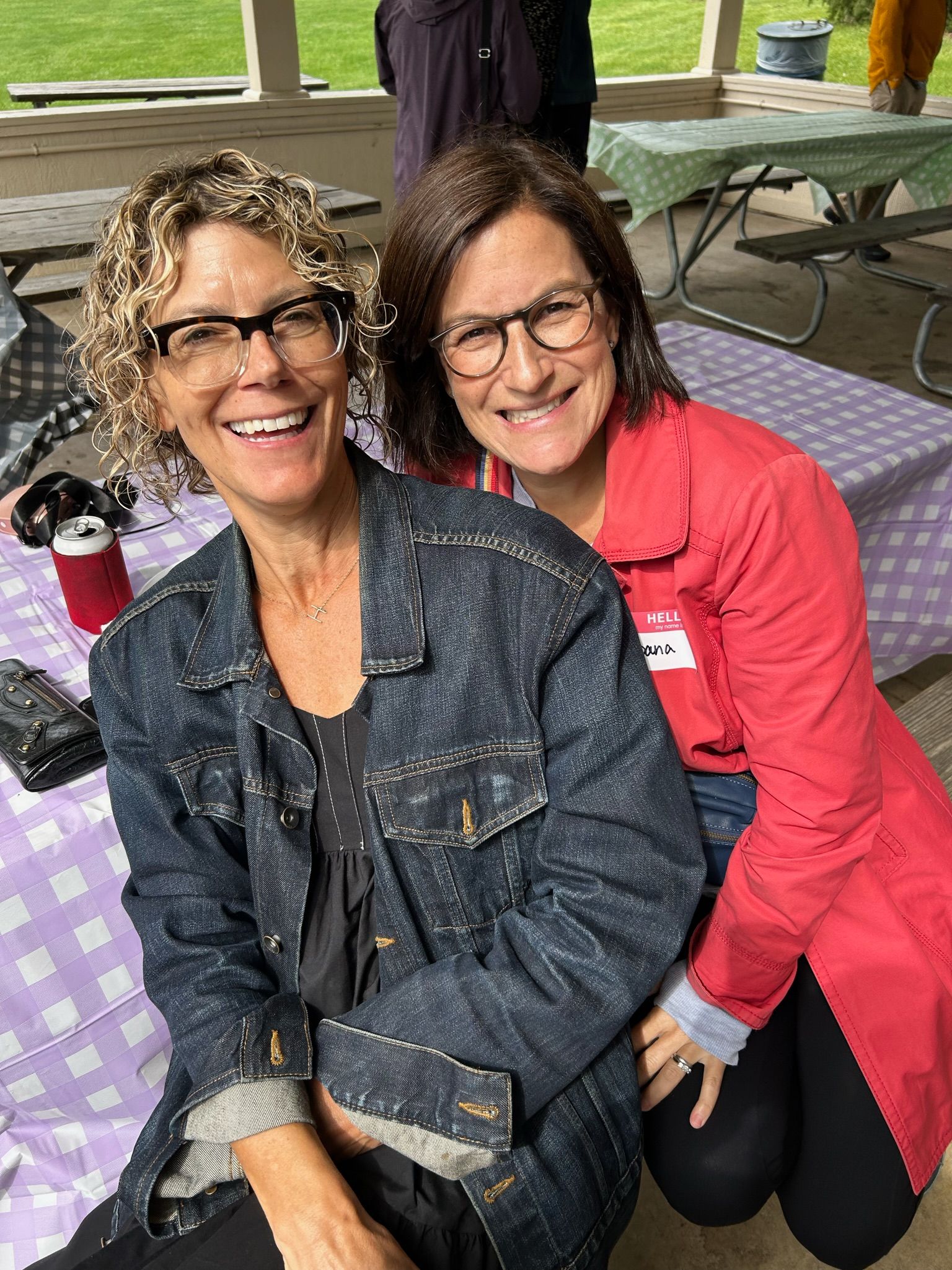 Two women are posing for a picture together at a picnic table.