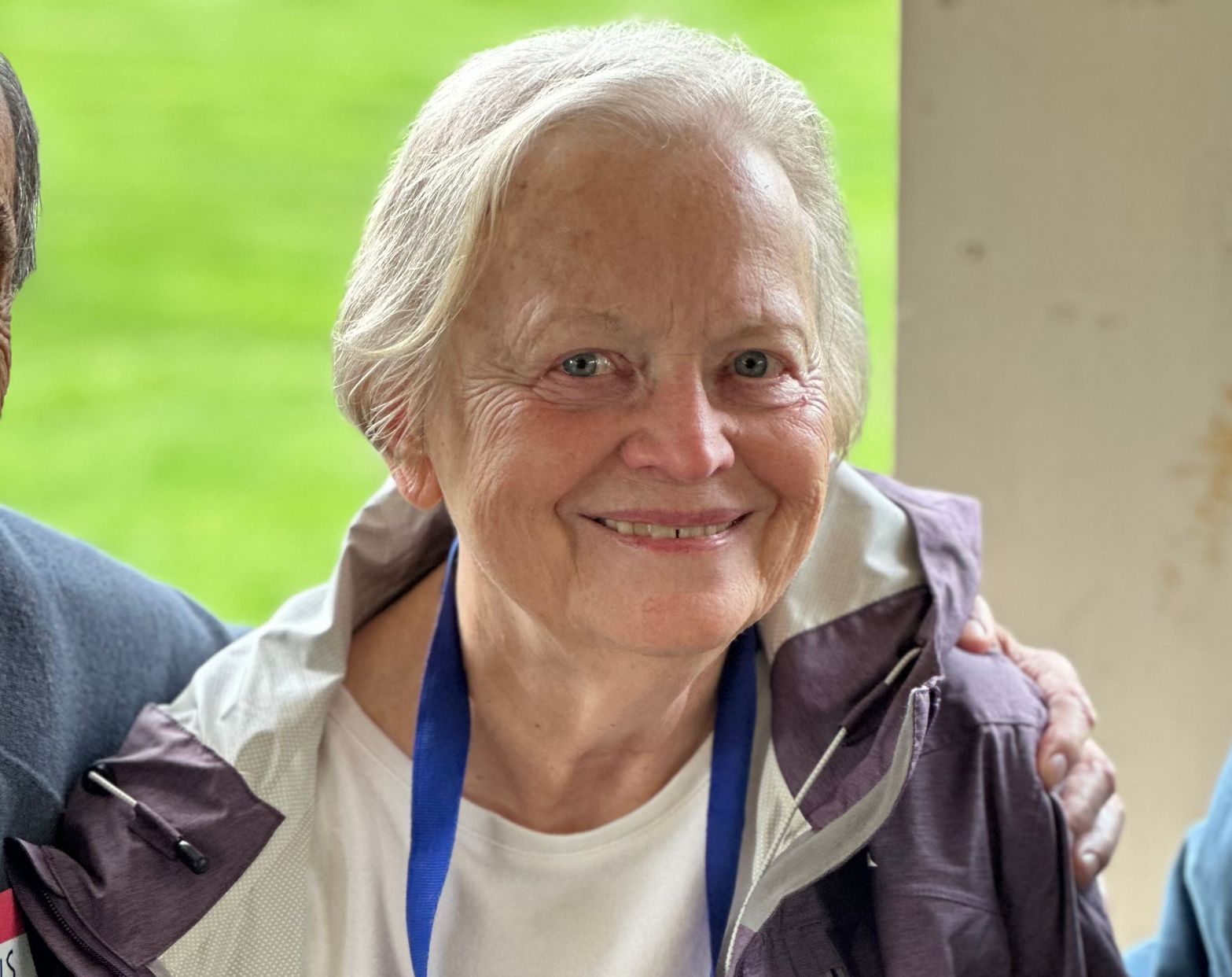 A woman wearing a purple jacket and a blue lanyard smiles for the camera.
