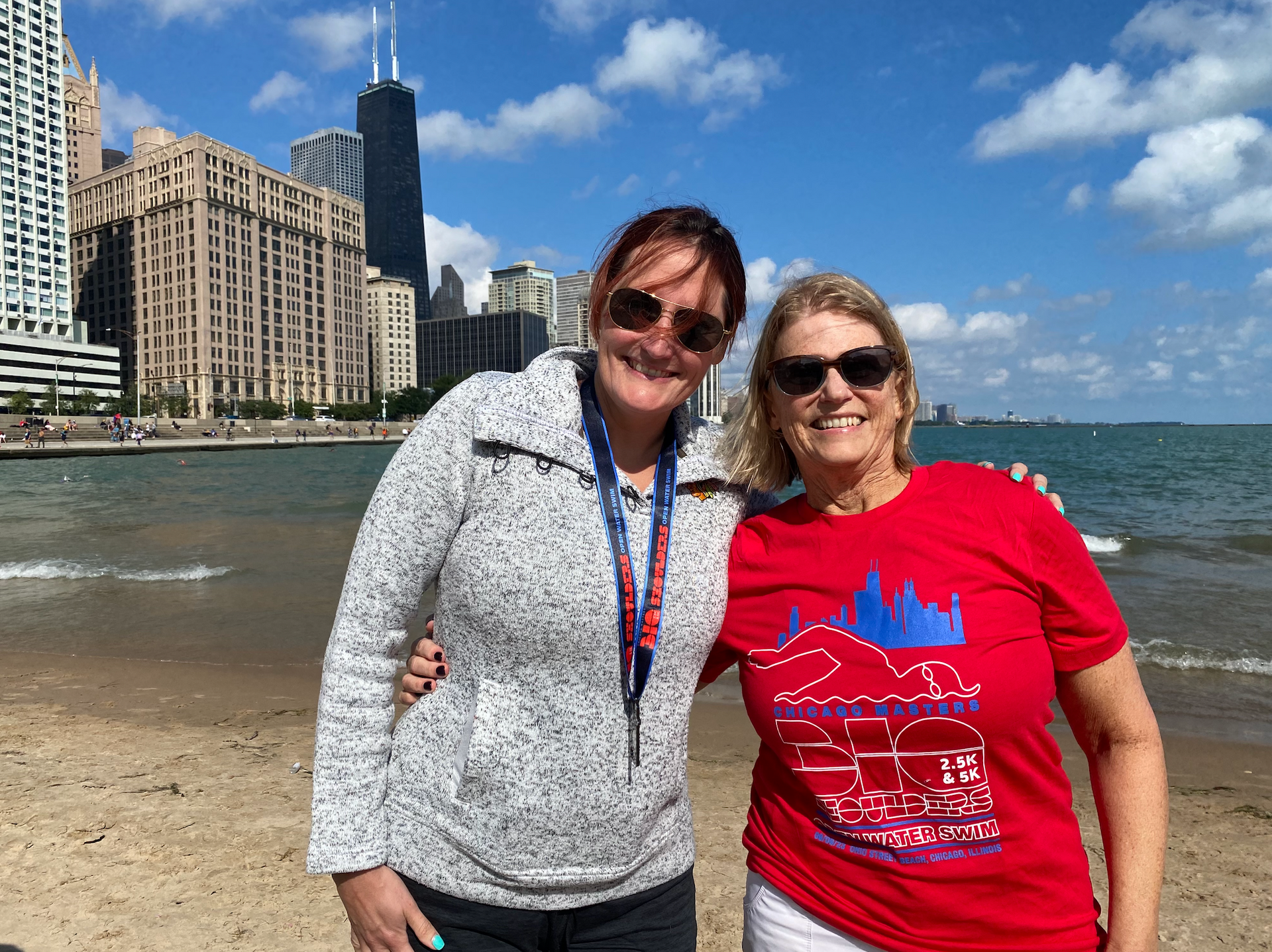 Two women are posing for a picture on the beach in front of a city skyline.