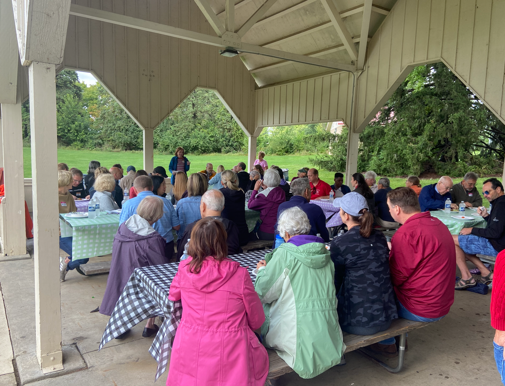 A group of people are sitting at picnic tables under a pavilion.