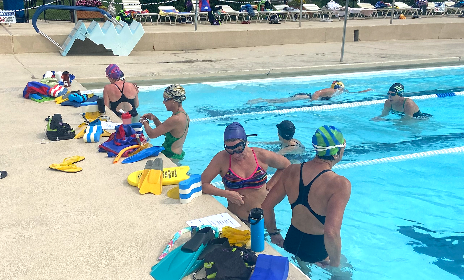 A group of women are sitting on the edge of a swimming pool.
