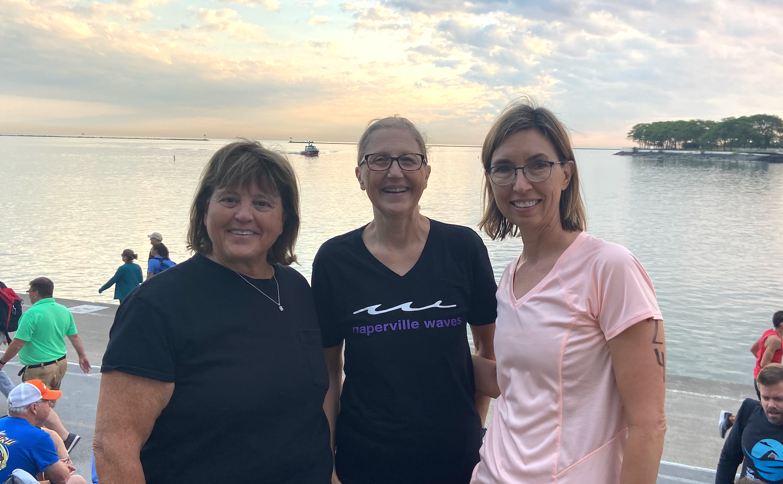 Three women are standing next to each other on a beach.