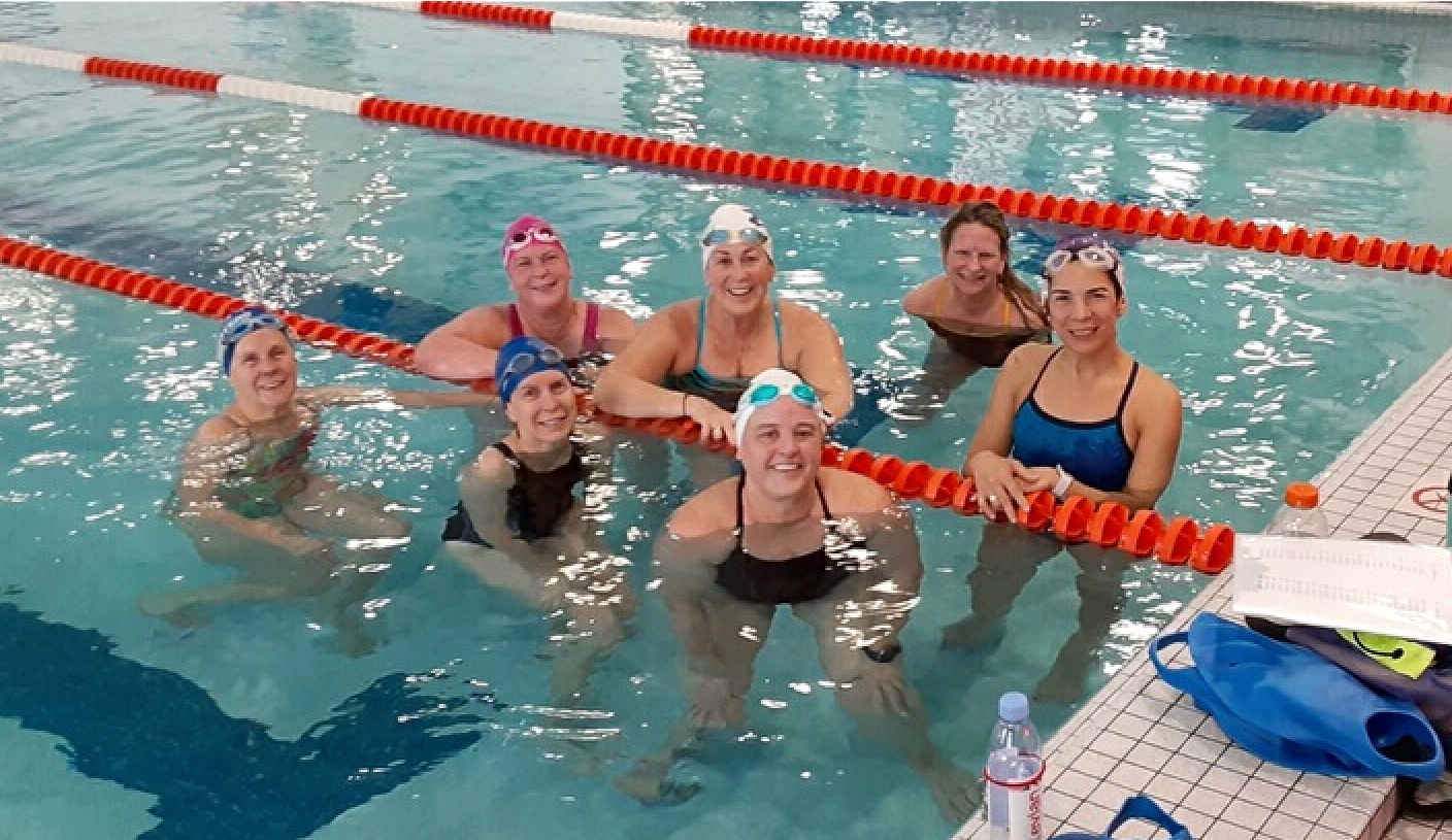 A group of women are posing for a picture in a swimming pool.