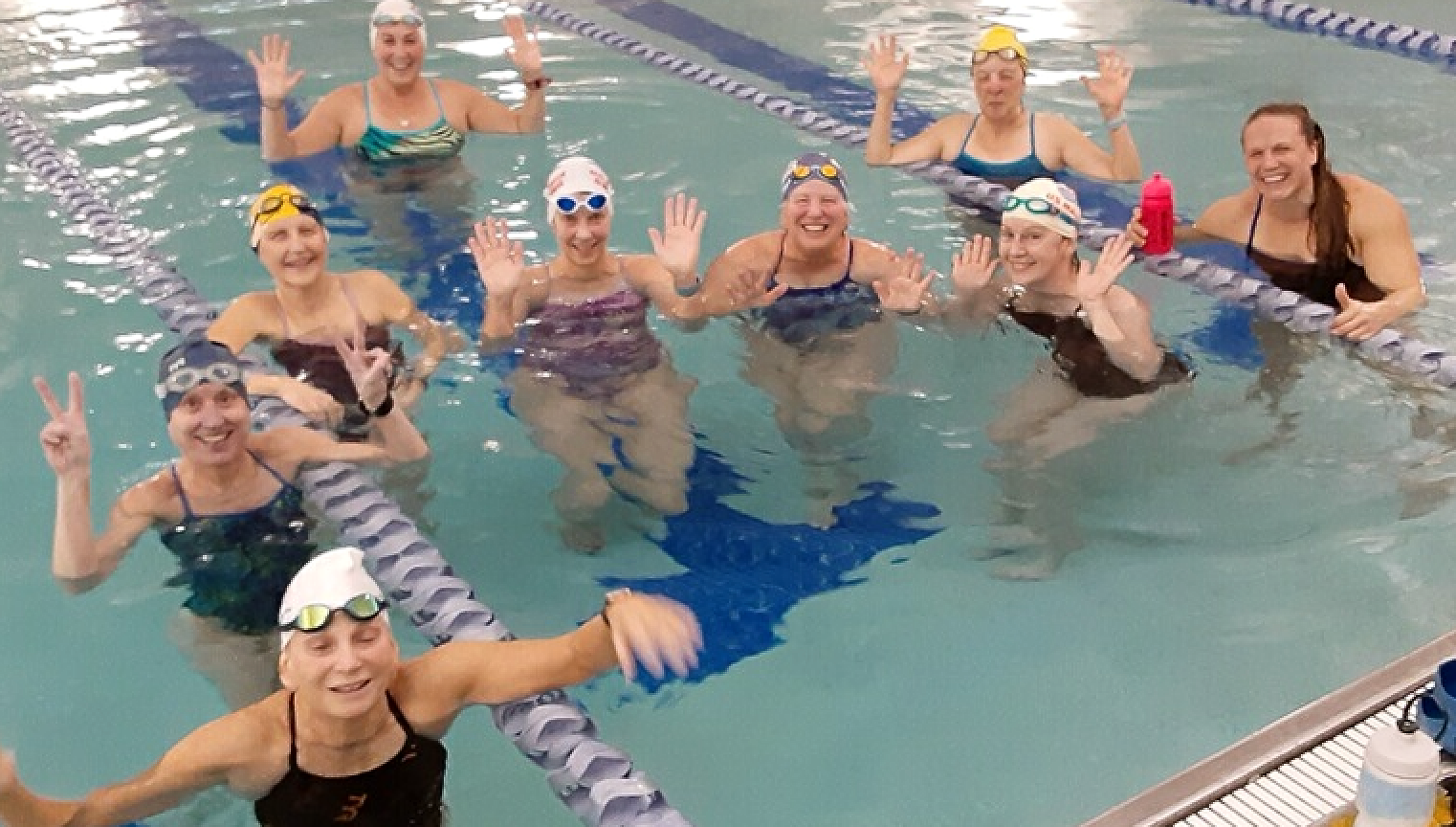 A group of women are posing for a picture in a swimming pool.