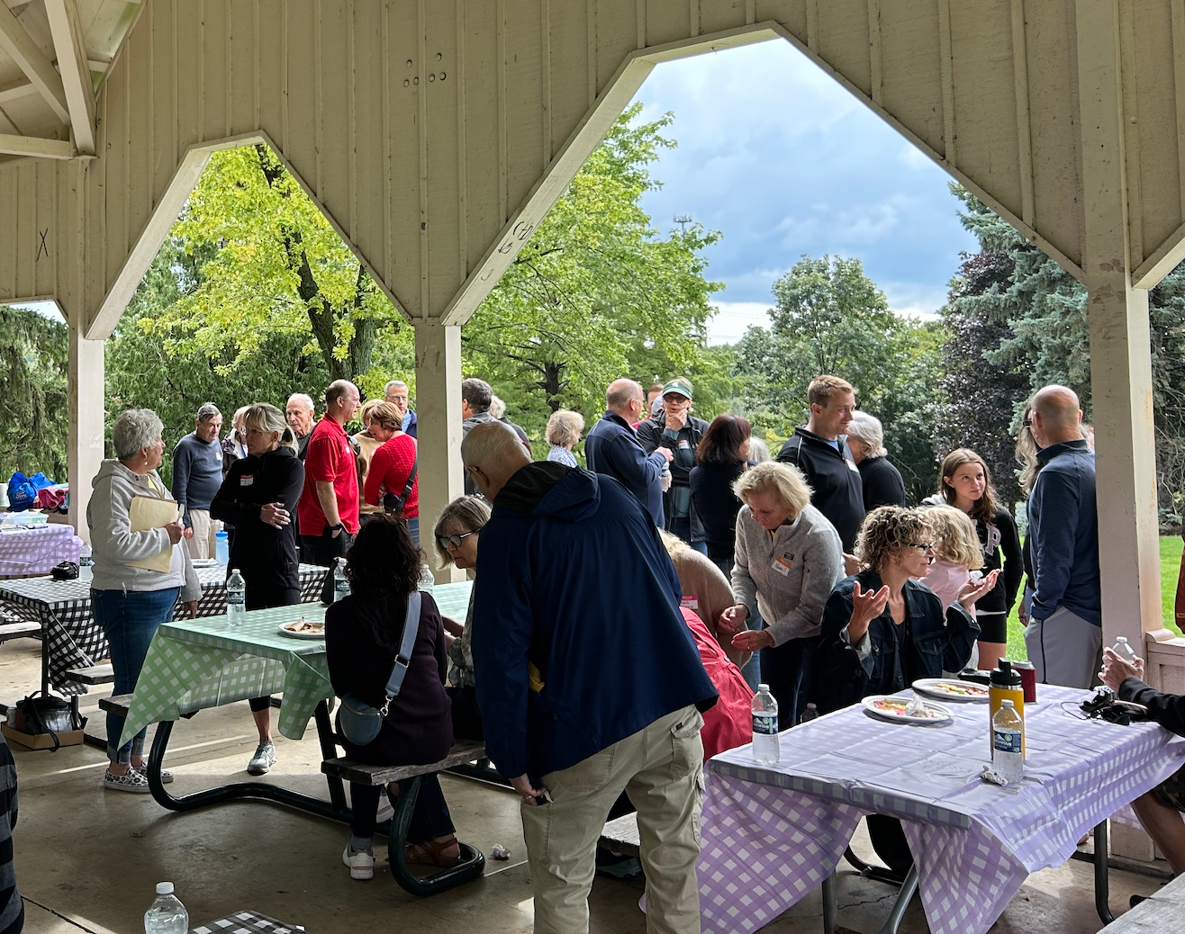 A group of people are standing around tables in a pavilion.