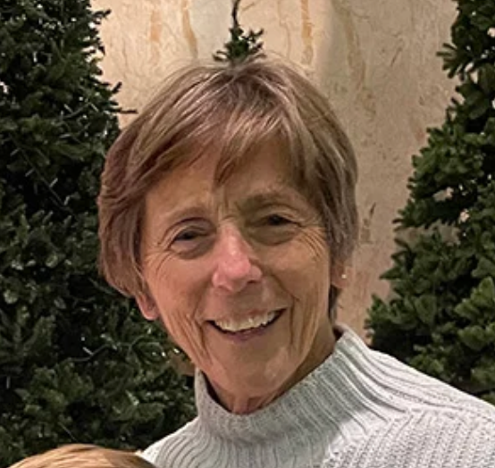 A woman in a sweater is smiling in front of a christmas tree.