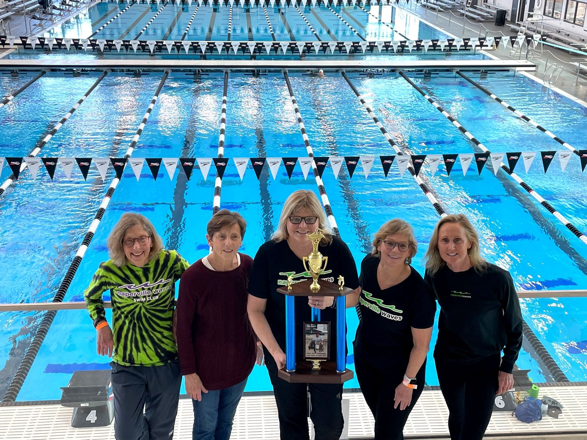A group of women are standing in front of a swimming pool holding a trophy.