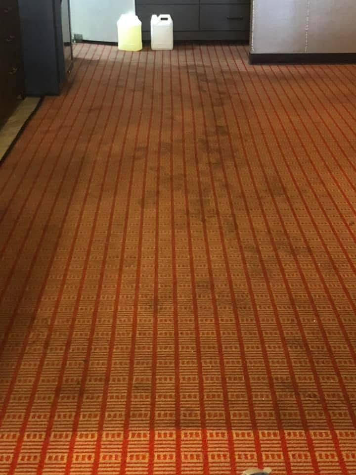 Carpeted hallway with patterned orange floor and two white jugs near dark cabinets at the far end