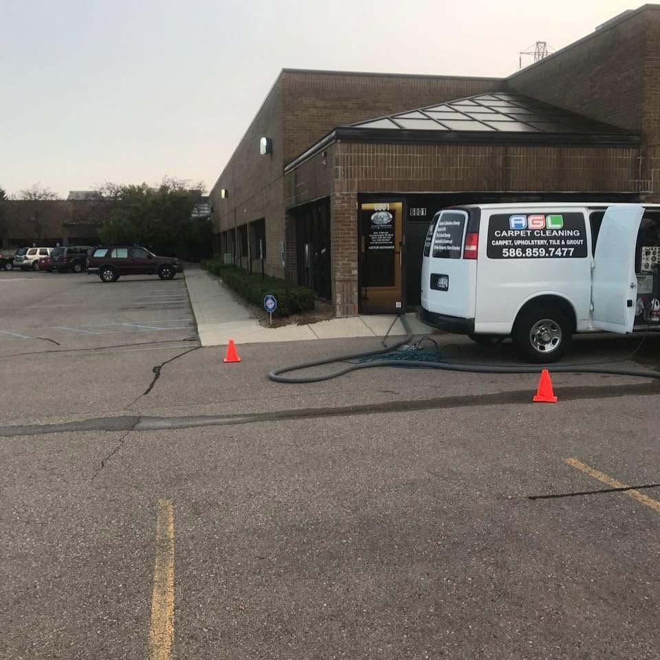 Commercial van parked outside a brick building, with orange cones and a hose on the pavement.