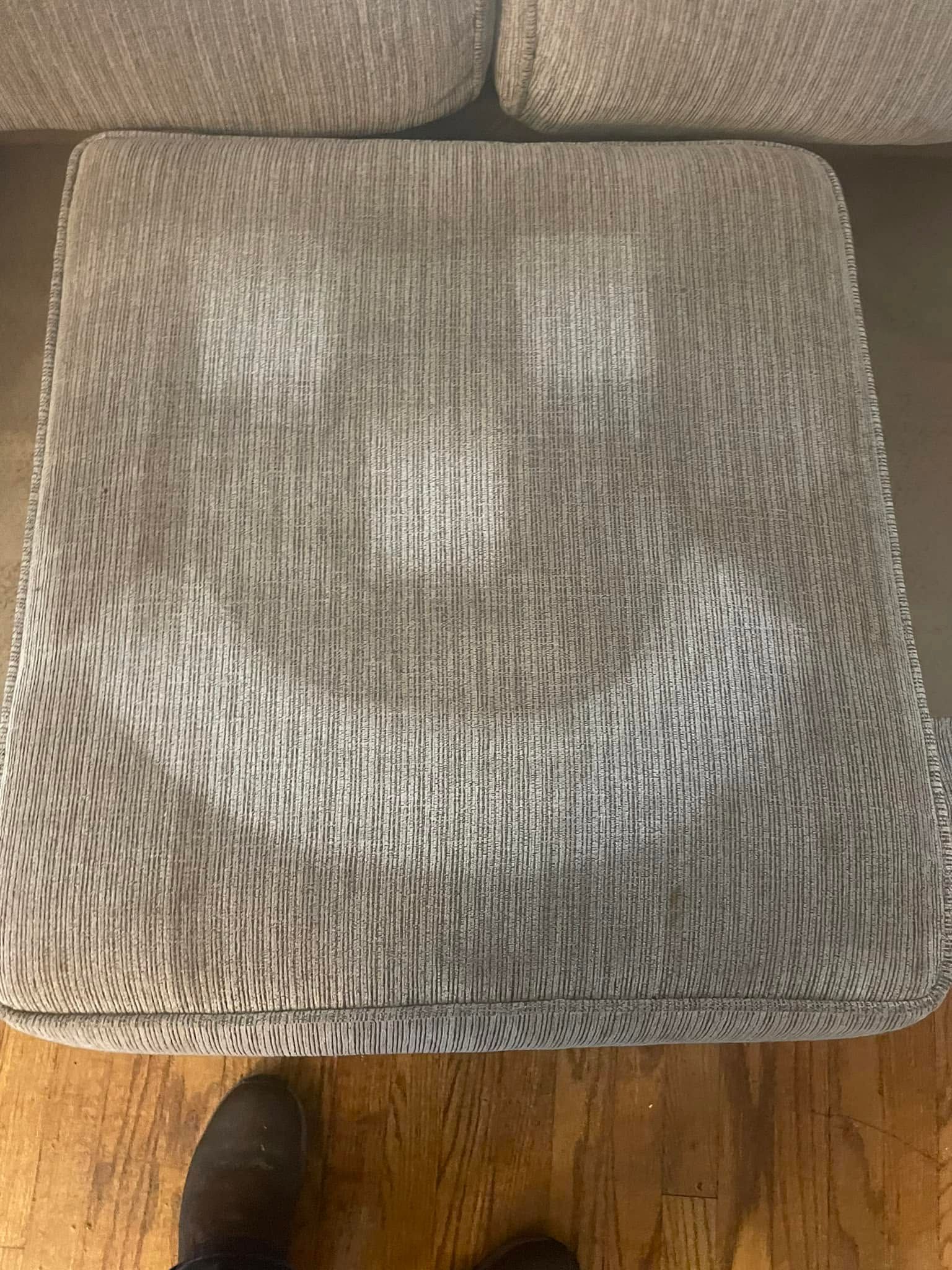 Gray woven upholstered chair seat viewed from above, with a tan floor and shoe visible at the bottom edge