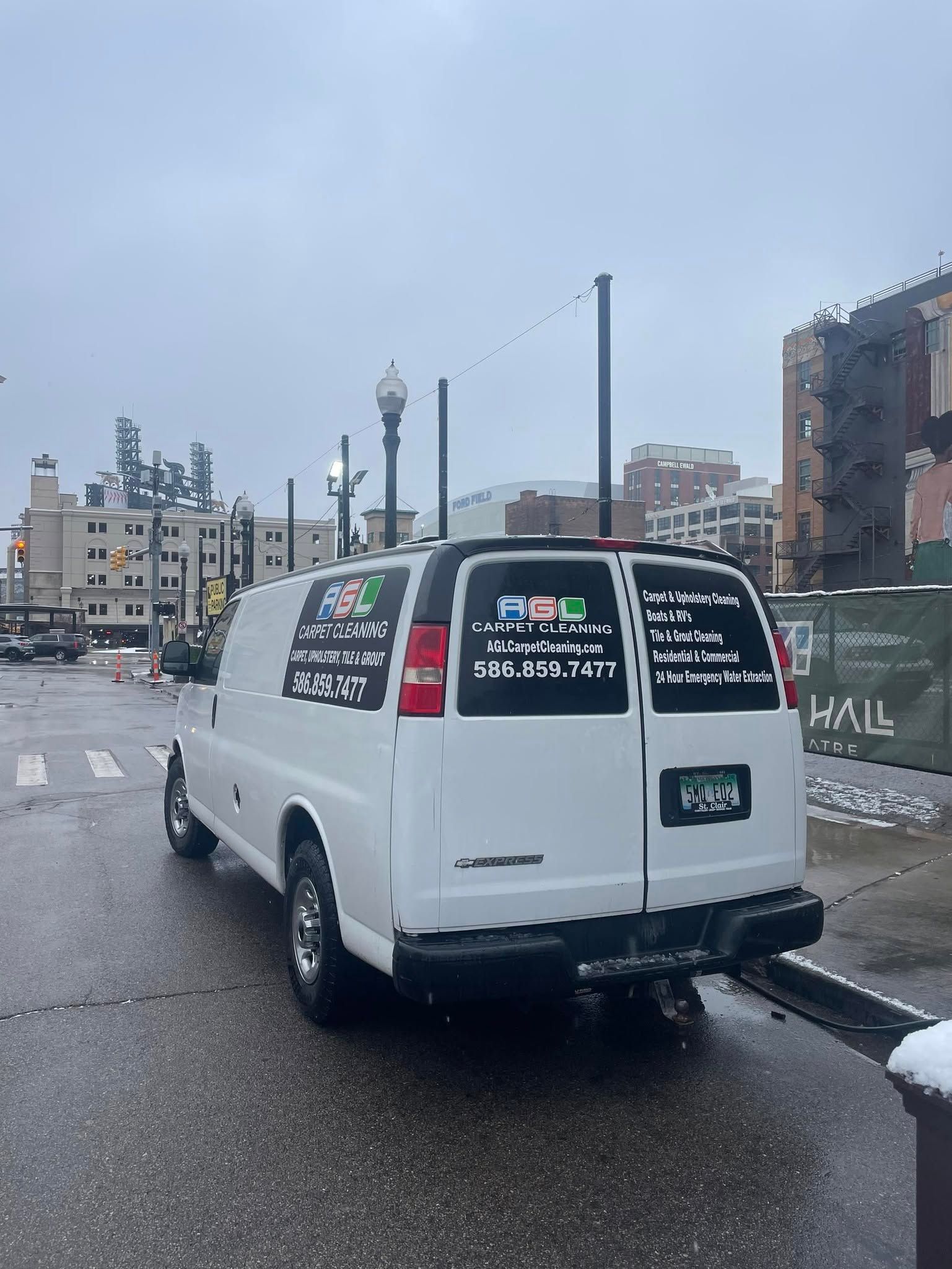 White van parked on a wet city street beside buildings and a canal, rear view visible.