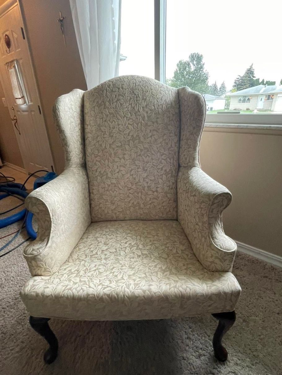 Light beige upholstered wingback armchair by a window on beige carpet