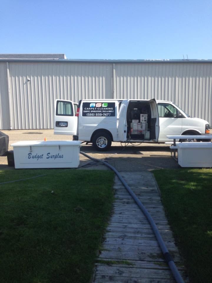 White service van with open doors parked outside a metal building near a grassy lawn and walkway.