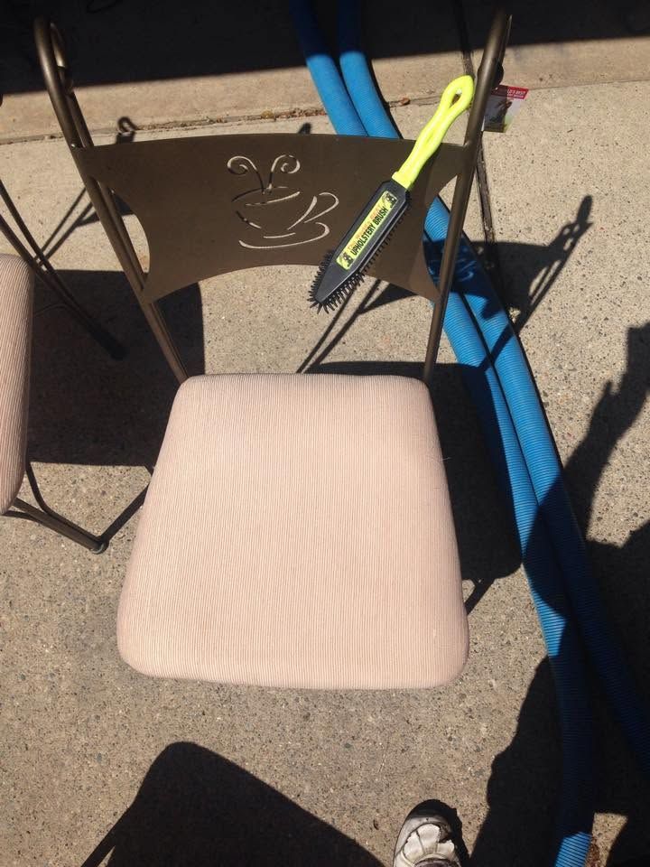 Pink cushioned chair on a patio with a black metal table and a yellow-handled tool nearby.