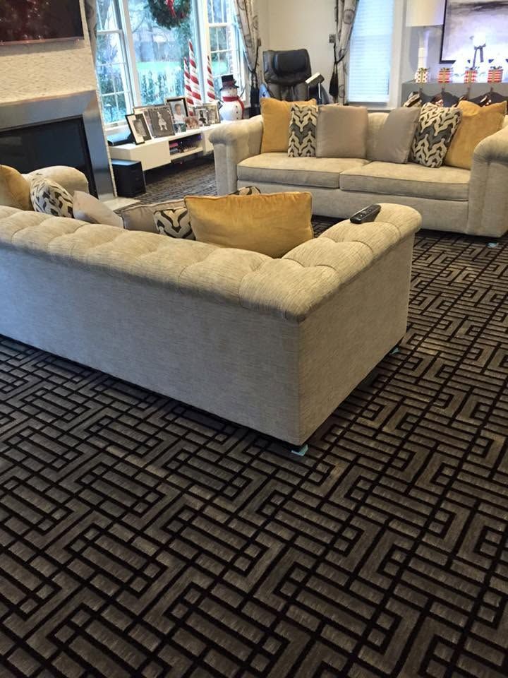 Modern living room with two beige sofas, patterned carpet, fireplace, and large windows