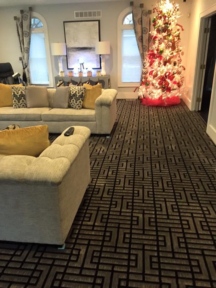 Cozy living room with cream sofas, patterned rug, and a lit red-and-white Christmas tree by the window.