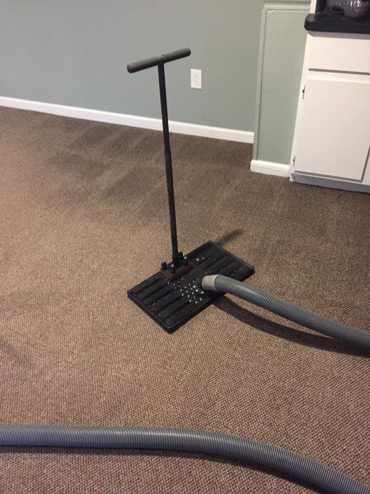 Carpeted room with a black hand pump and vacuum hose on the floor near a wall and cabinet.