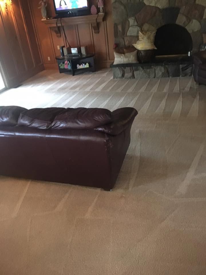 Living room with beige carpet, brown leather sofa, and stone fireplace under a wall-mounted TV