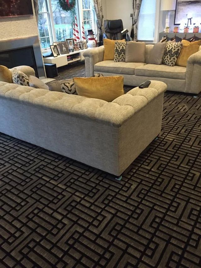 Modern lounge with beige sofas, patterned carpet, and a fireplace near large windows.