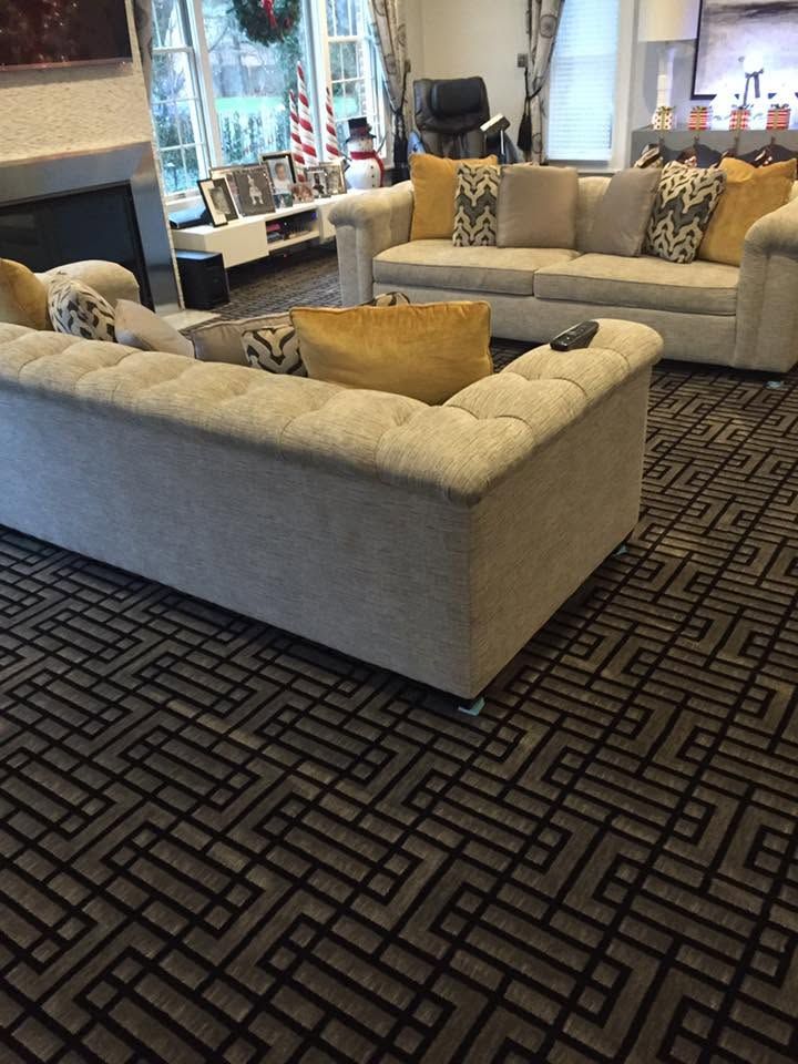 Modern living room with gray sofas, patterned black carpet, beige pillows, and a fireplace by a window.